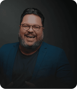 Um painel digital em cinza e preto com um homem sorridente de óculos, barbudo e camisa social azul. Ele aponta para o centro do painel, onde há vários cartões com textos como 'Equipe engajada', 'Clientes agendados' e 'Meta de vendas batida!'. Na parte inferior, há botões com os textos 'Ligar para cliente', 'Chamar no WhatsApp', 'Agendar tarefa', 'Registrar novo contato' e 'Ver convite'.